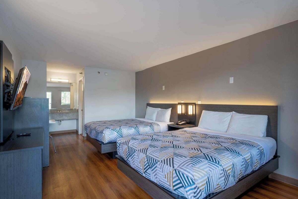 Habitación de hotel con dos camas, un escritorio y un baño visible al fondo.