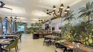 A spacious restaurant with multiple dining tables, chairs, and a large mural of tropical foliage on the wall. - Protea Hotel by Marriott Livingstone (Livingstone)