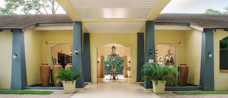 A hotel entrance with a covered walkway, large potted plants, and a chandelier.