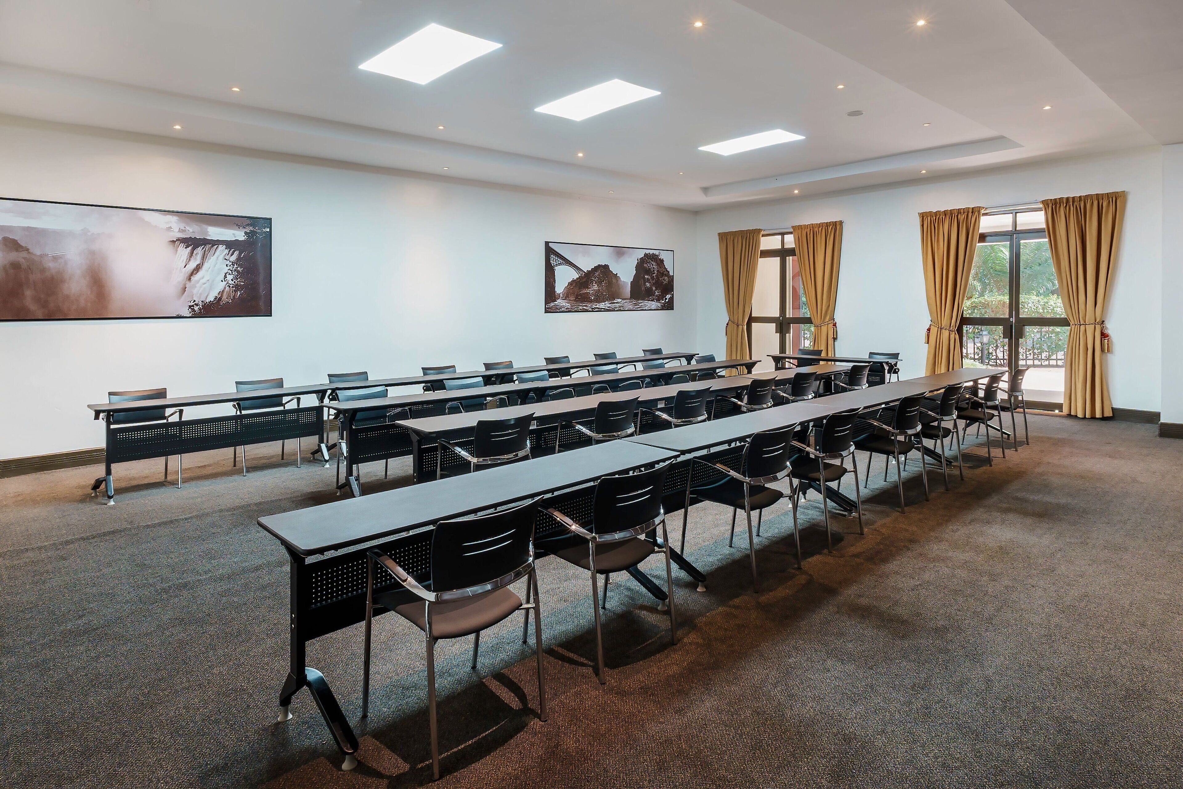 A conference room with long tables and chairs, large windows with curtains, and artwork on the walls.