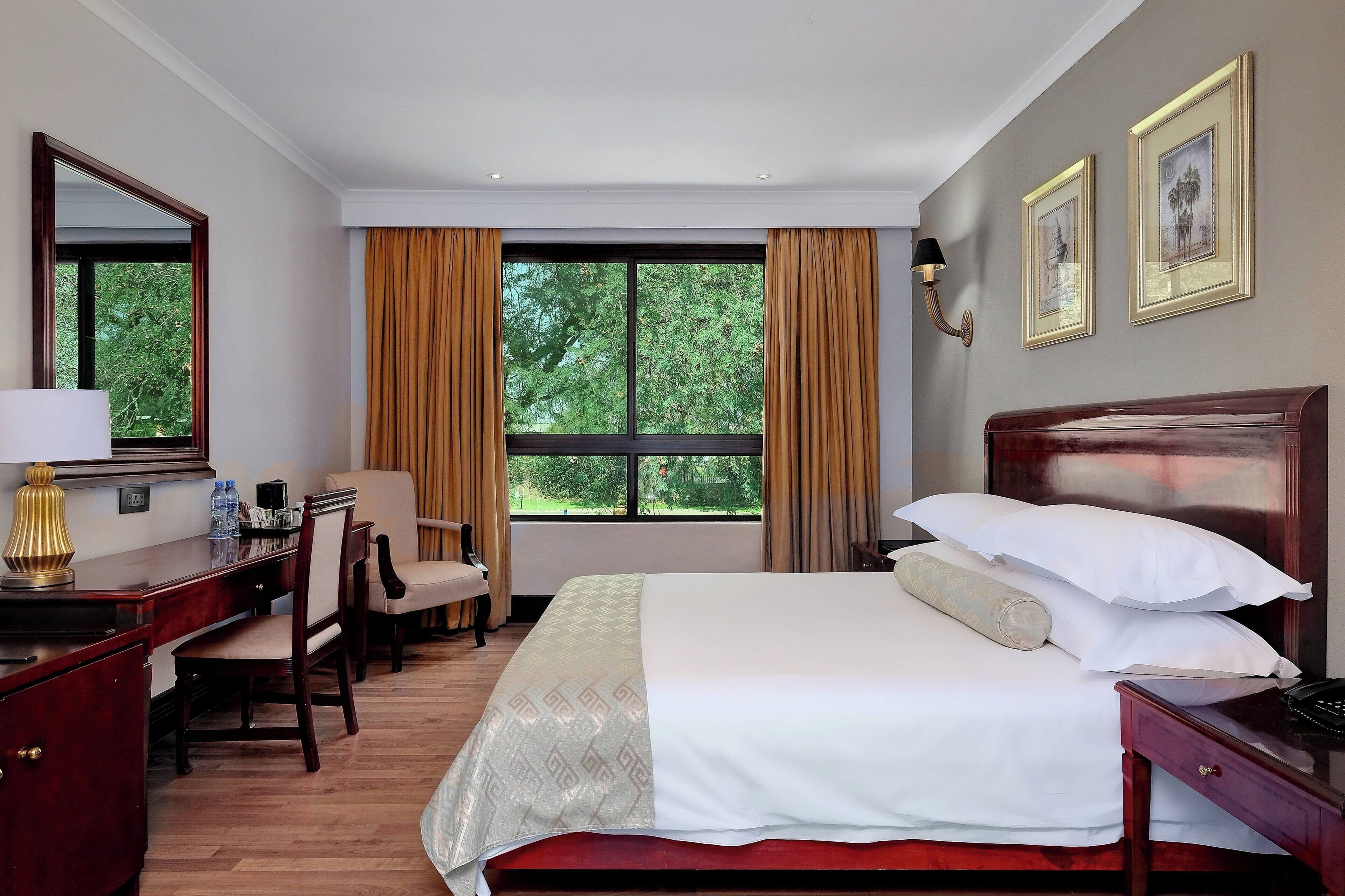 A hotel room with a bed, desk, chair, and a large window with curtains.