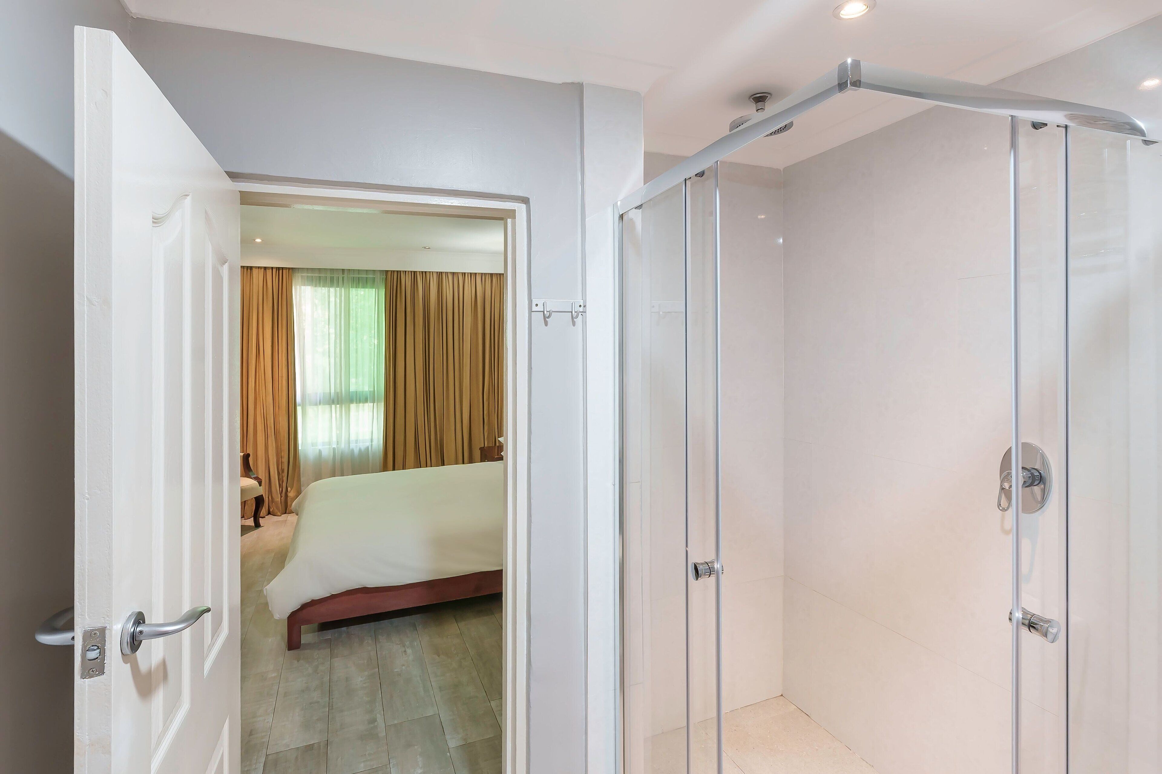 A hotel room with a bed, a shower area, and a door leading to another room.