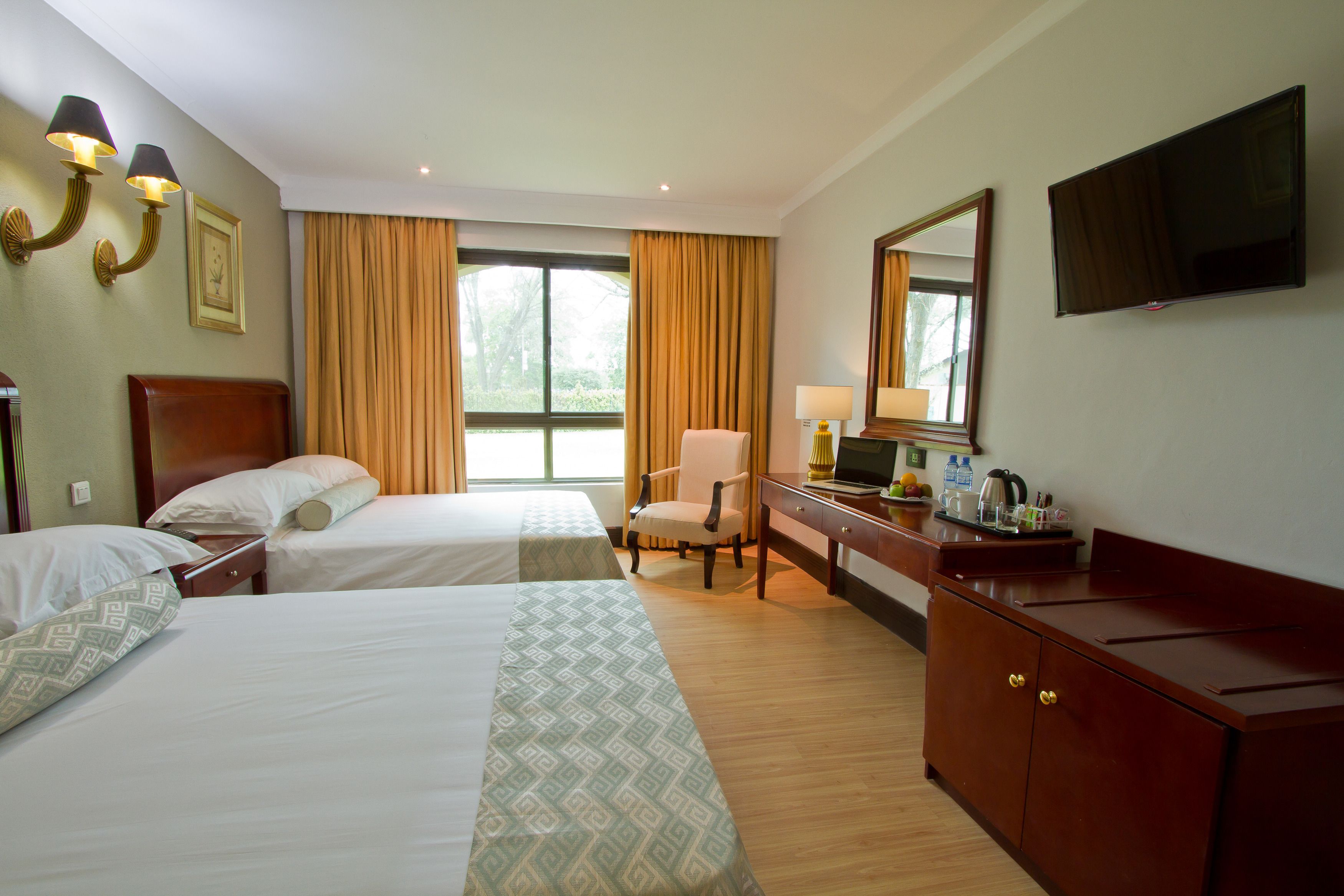 A hotel room with two beds, a desk with a TV, a chair, and a window with curtains.