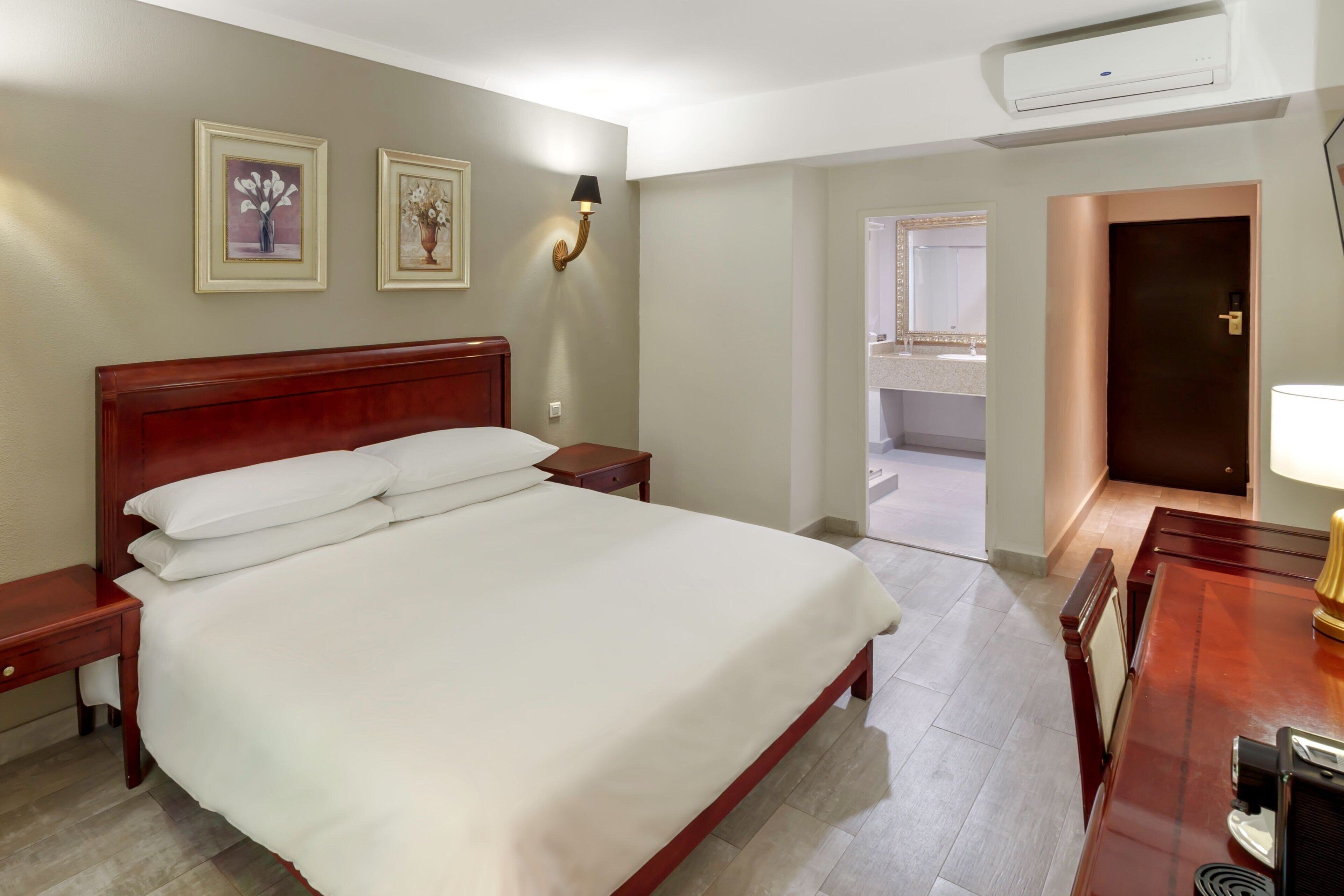 Habitación de hotel con una cama grande, mesitas de noche, un escritorio con lámpara y cuadros en la pared.