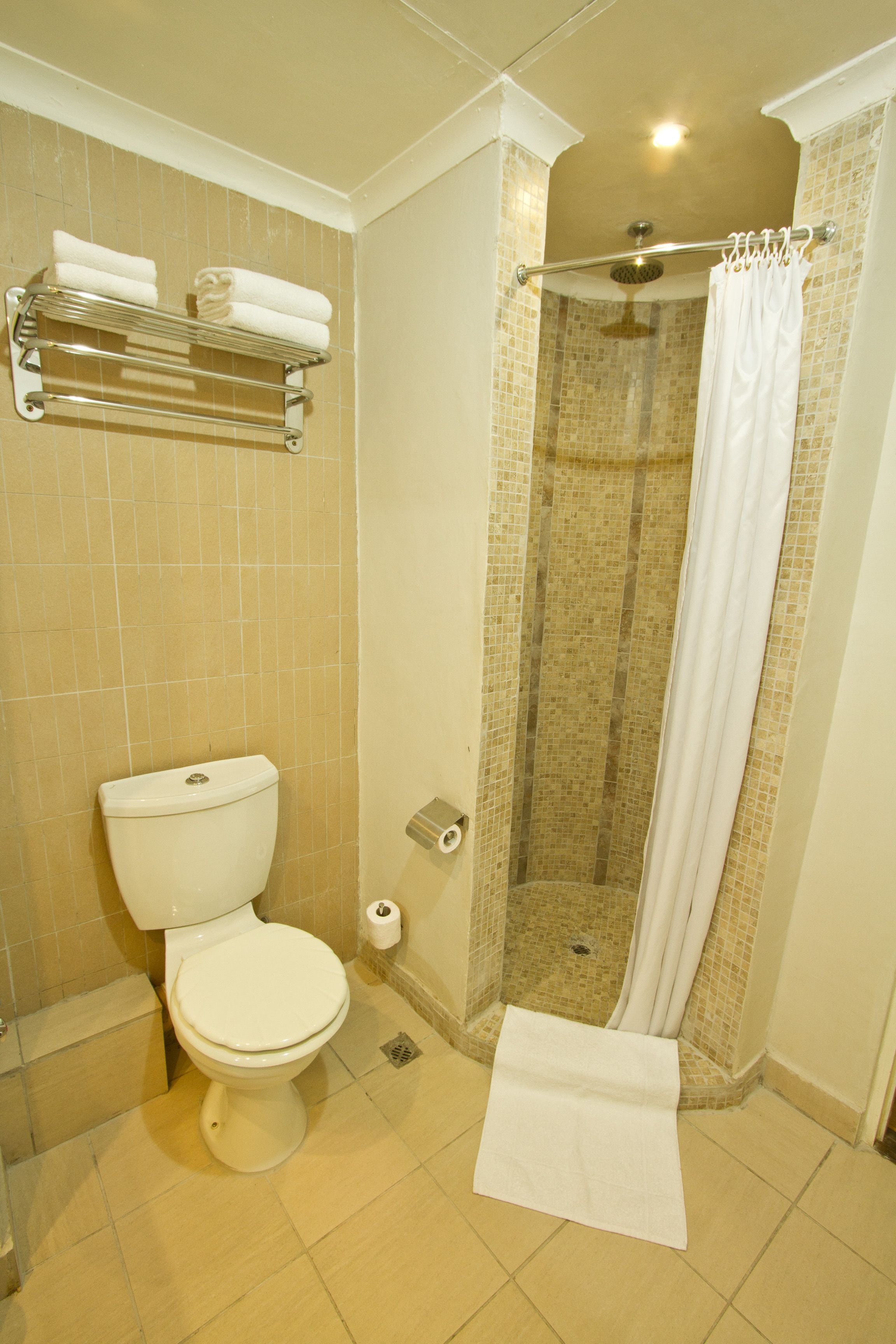 Un baño con inodoro, ducha con puerta de cristal y toallero con toallas dobladas.