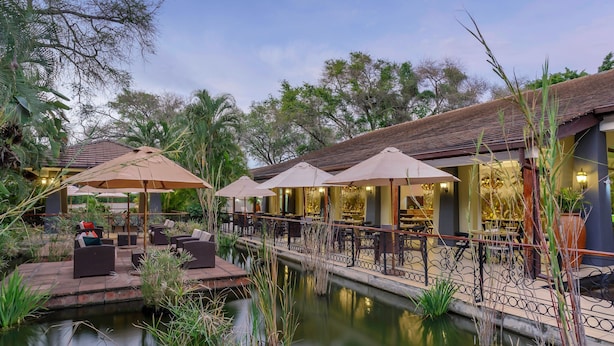 A serene outdoor seating area with umbrellas, a small pond, and a restaurant with outdoor seating. - Protea Hotel by Marriott Livingstone (Livingstone)