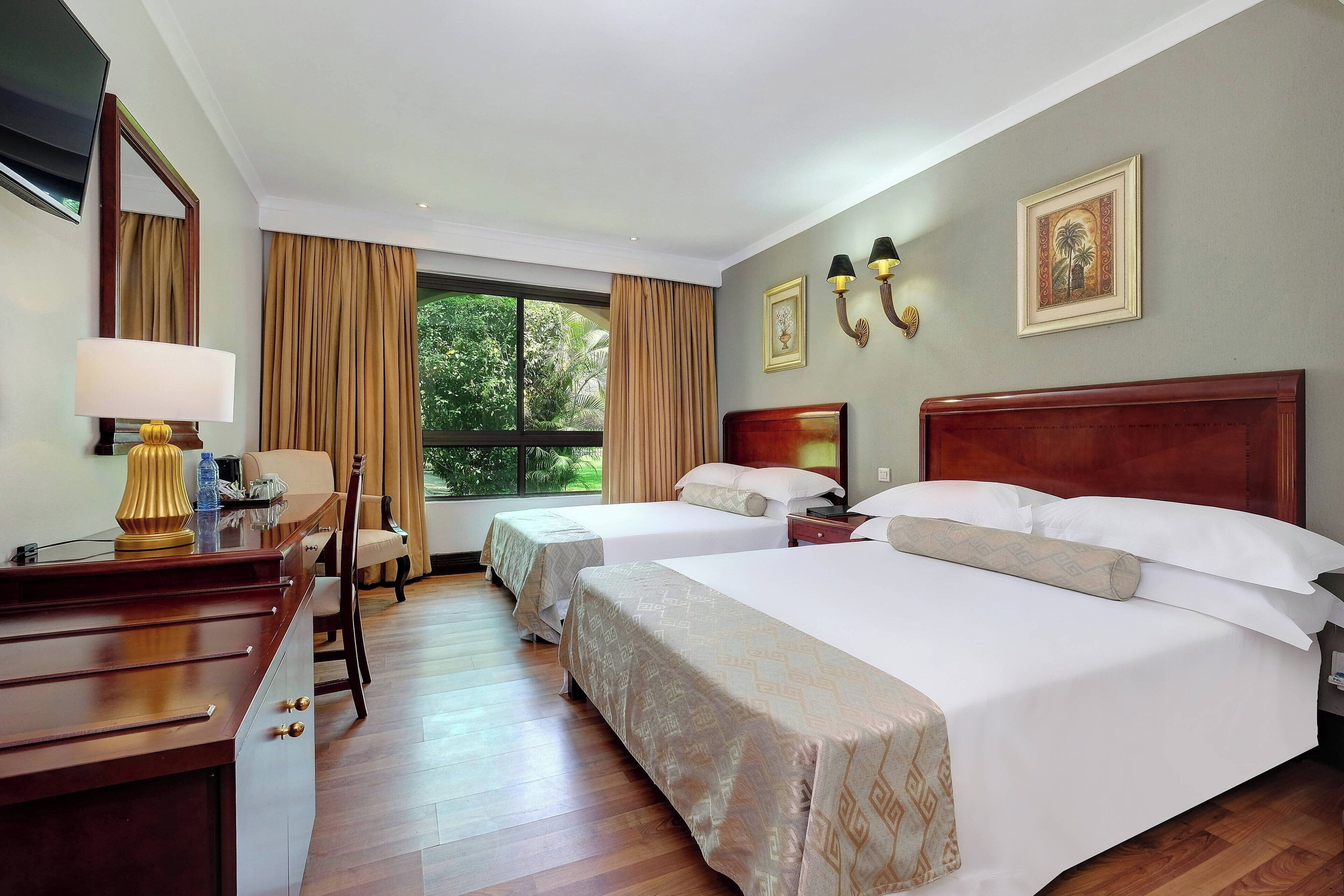 A hotel room with two beds, a desk, a chair, a TV, and a window with curtains.