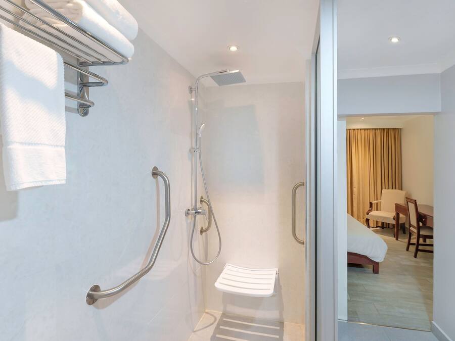 Une salle de bain moderne équipée d’une douche, de barres d’appui, d’un porte-serviettes et d’un petit banc.