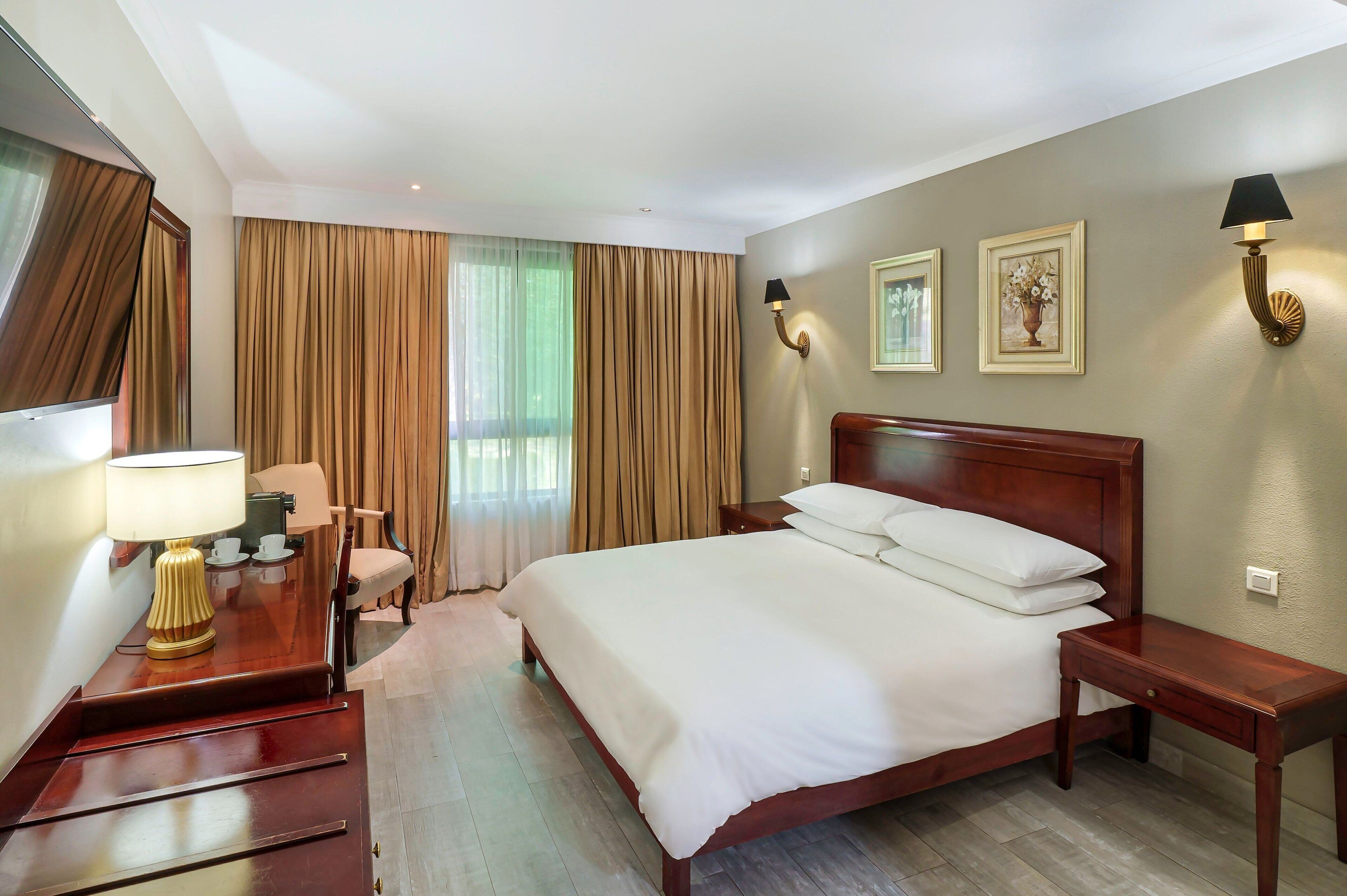Habitación de hotel con una cama grande, un escritorio con lámpara, una silla y dos lámparas de pared.