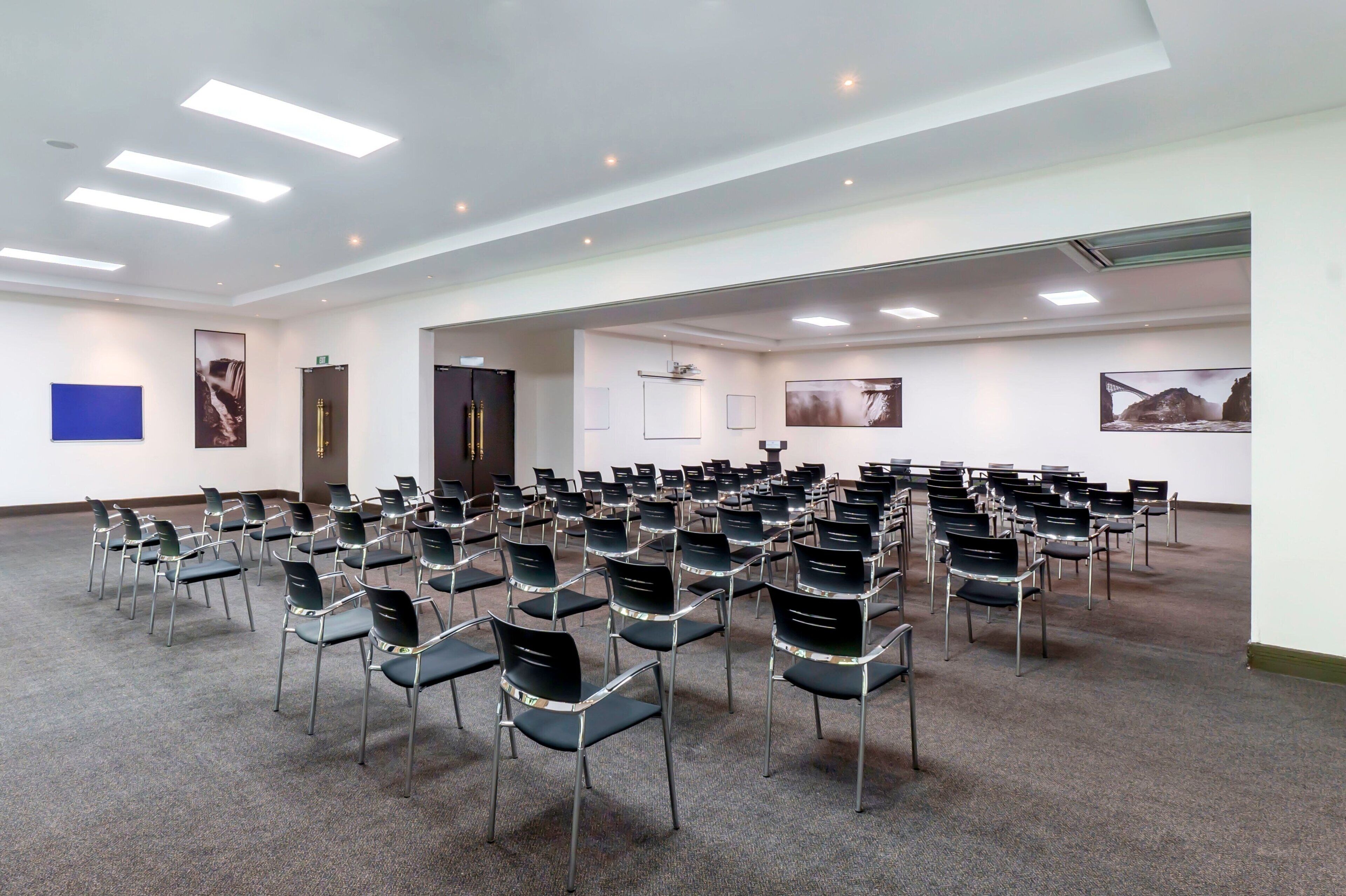 A conference room with rows of chairs, white walls, and ceiling lights.