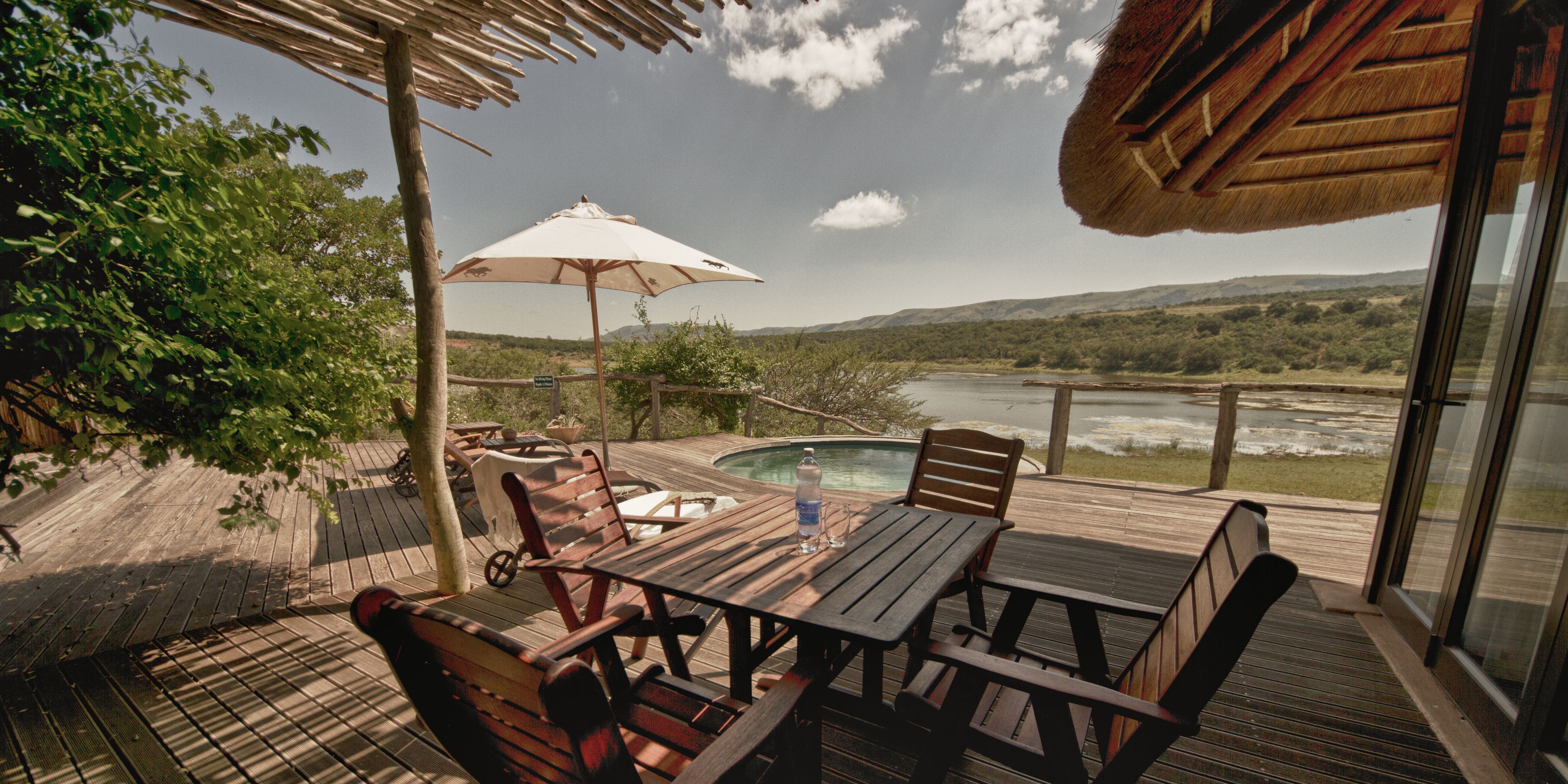 A wooden deck with outdoor furniture, a pool, and a scenic view of a lake and hills.