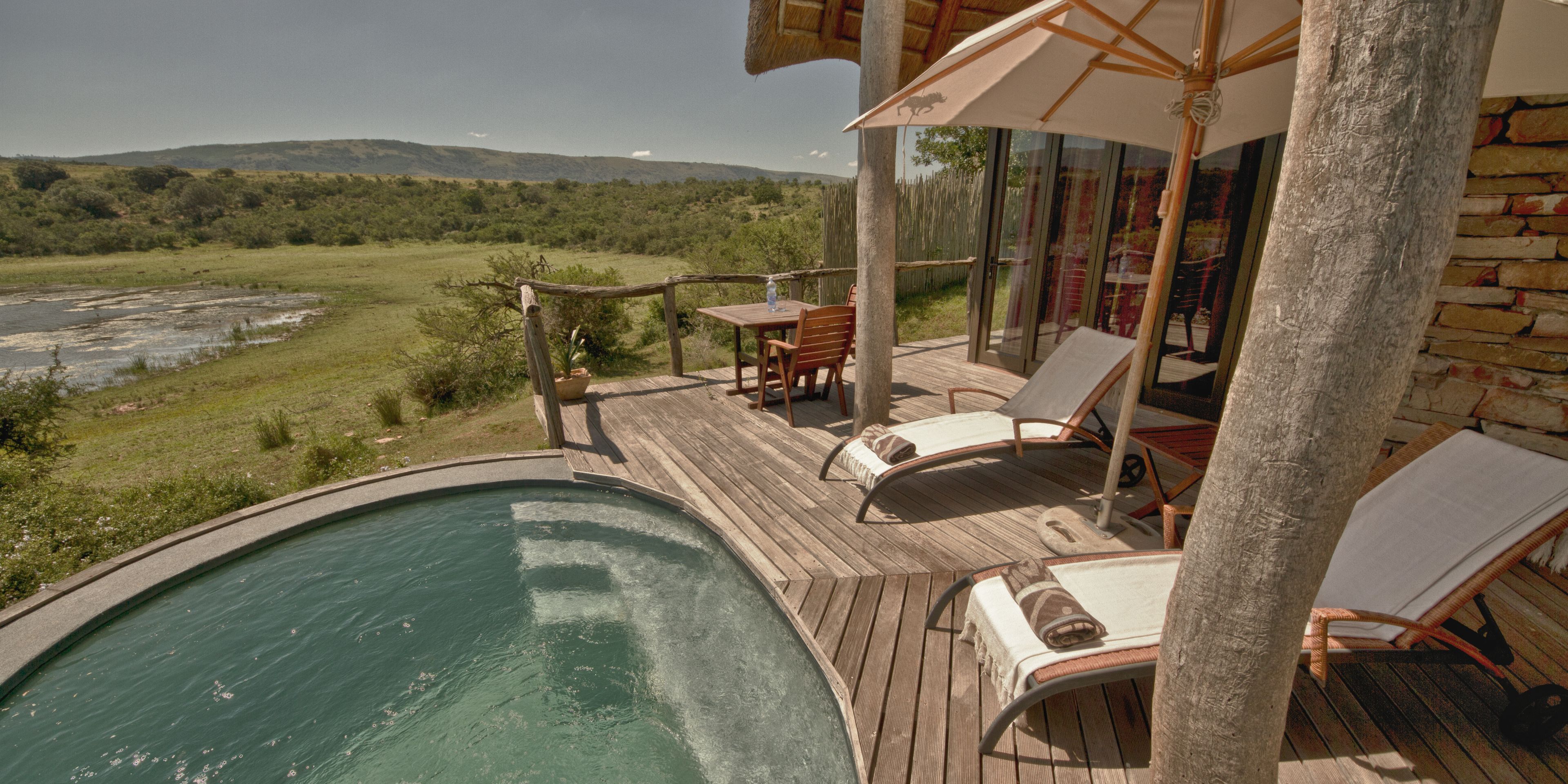 A poolside area with lounge chairs and a table, overlooking a natural landscape.