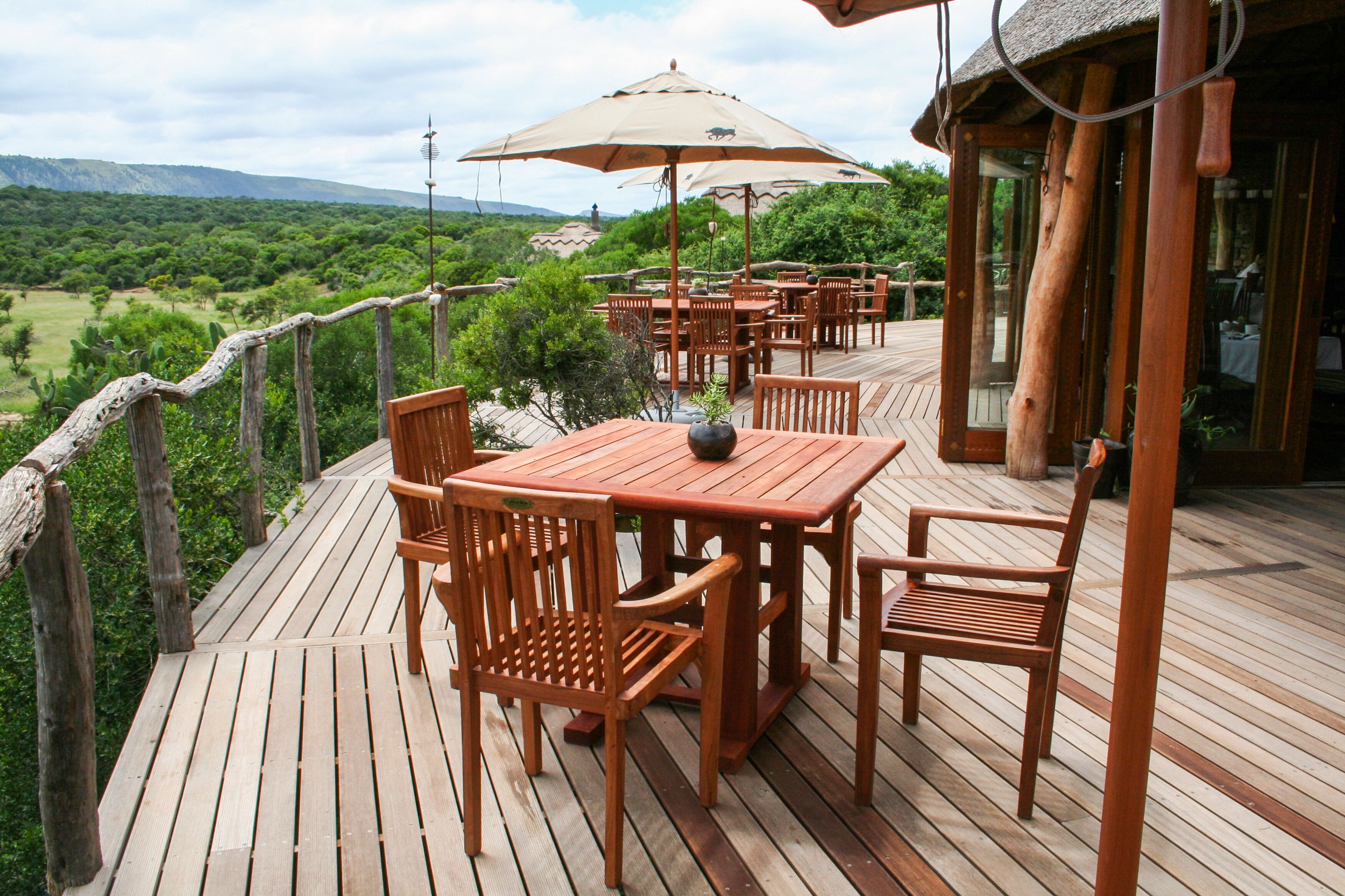 A wooden deck with outdoor seating, including tables and chairs, overlooking a lush landscape.