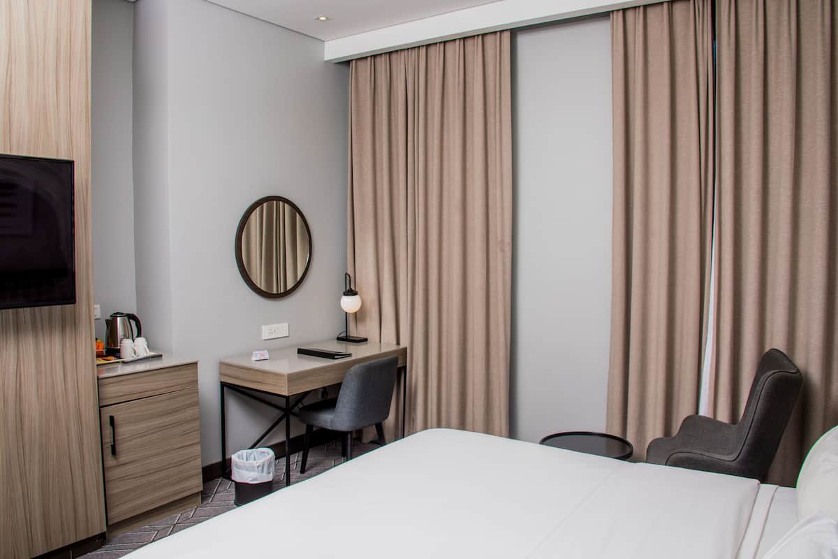 A hotel room with a bed, desk, chair, TV, and curtains.