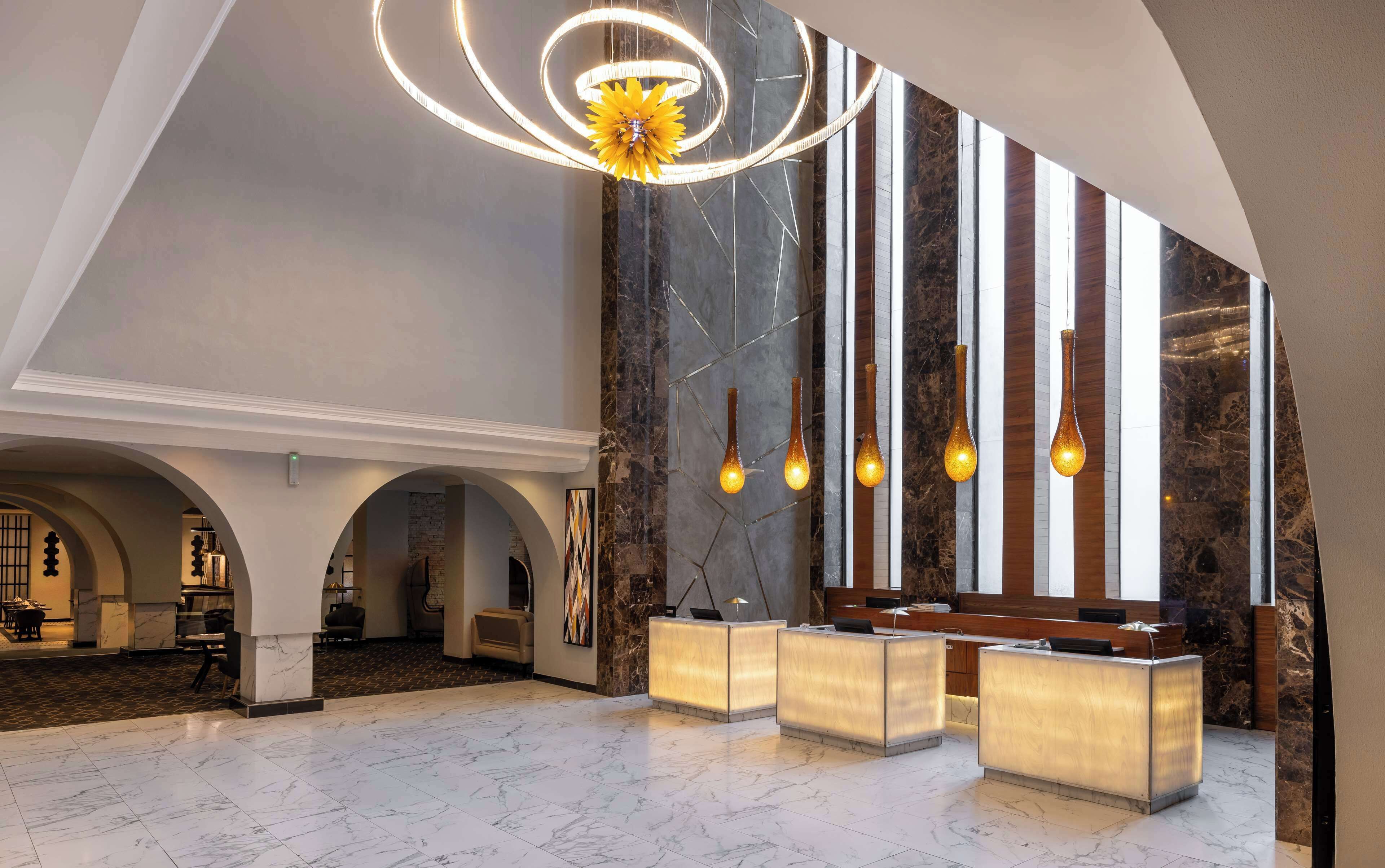 A spacious lobby with marble flooring, a modern reception desk, and a unique circular chandelier.