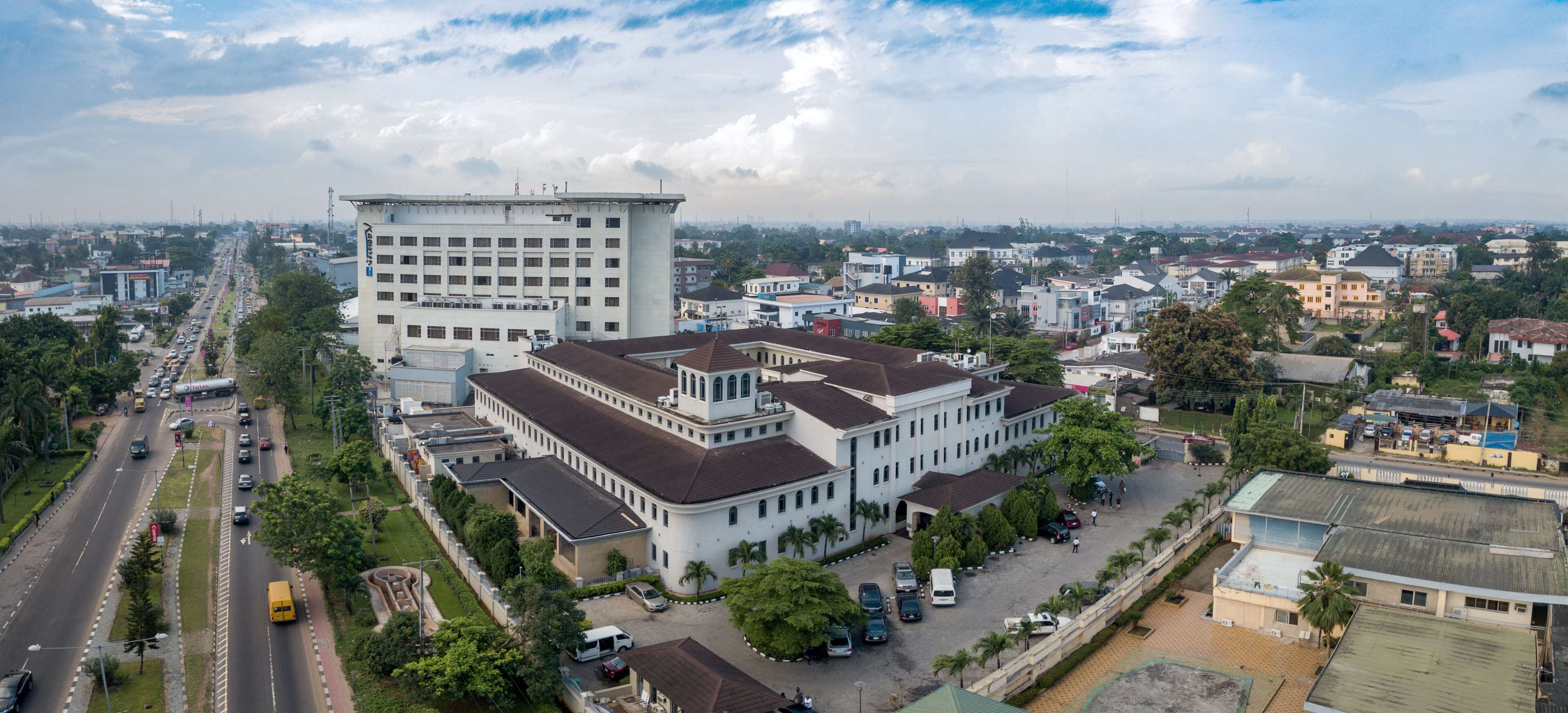 An aerial view of a large building complex with multiple structures, surrounded by roads and greenery.