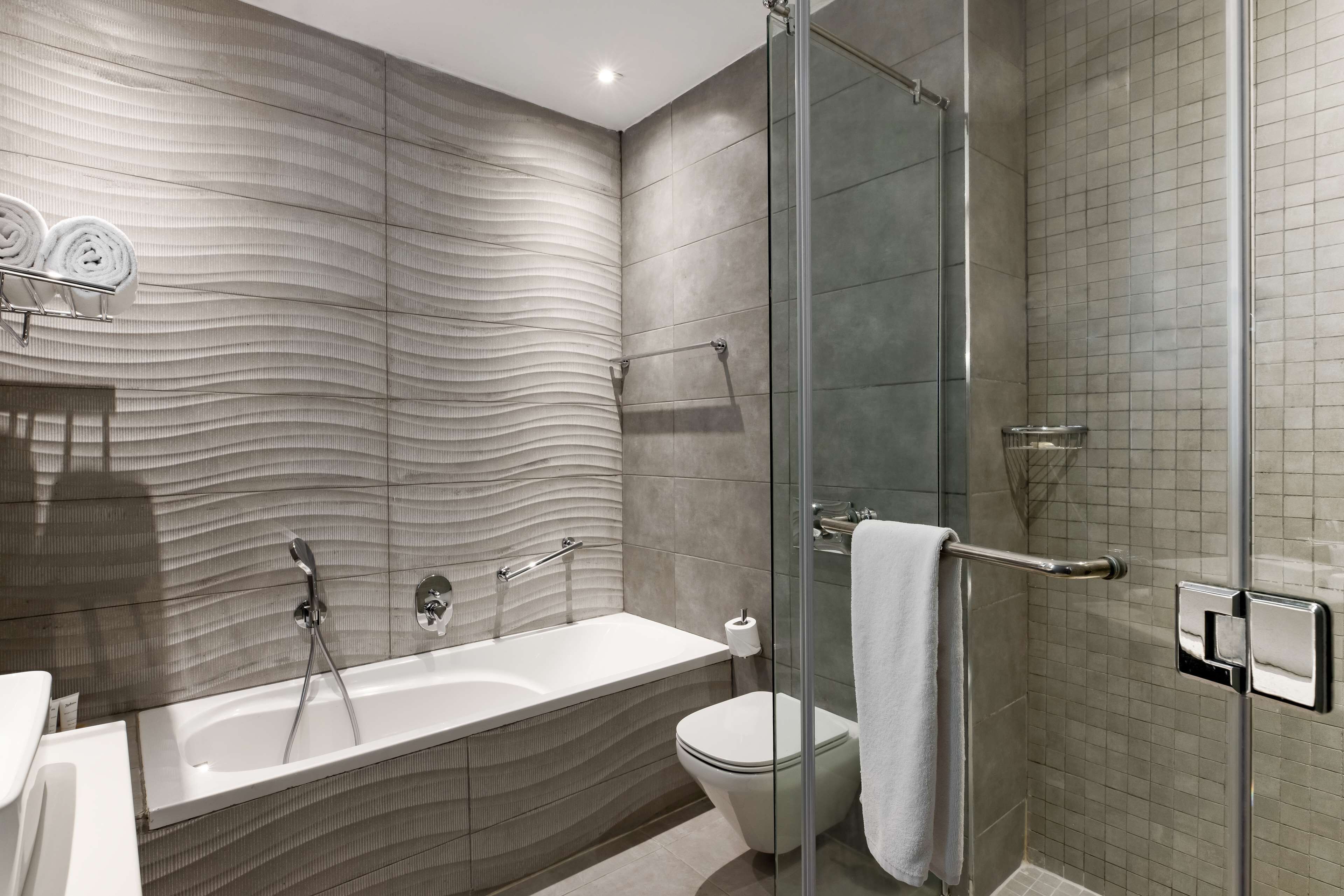 A modern bathroom with a glass-enclosed shower, a white bathtub, and a toilet.