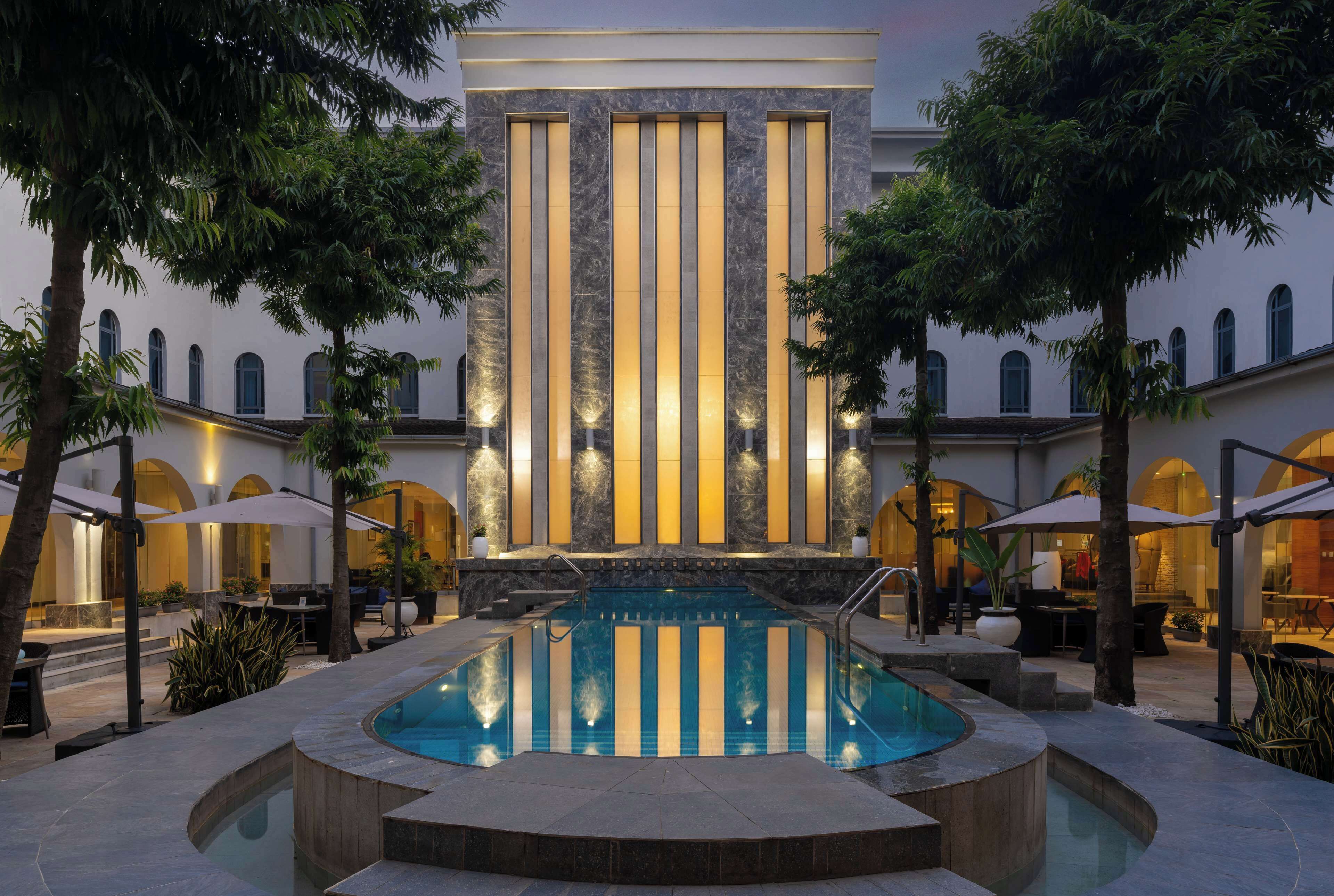 Un área de piscina con una fuente, rodeada de mobiliario exterior y palmeras.