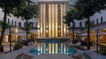 Un área de piscina con una fuente, rodeada de mobiliario exterior y palmeras.