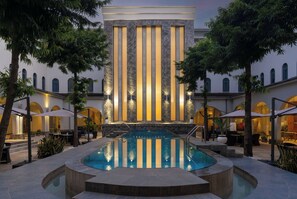 A pool area with a fountain, surrounded by outdoor seating and palm trees.