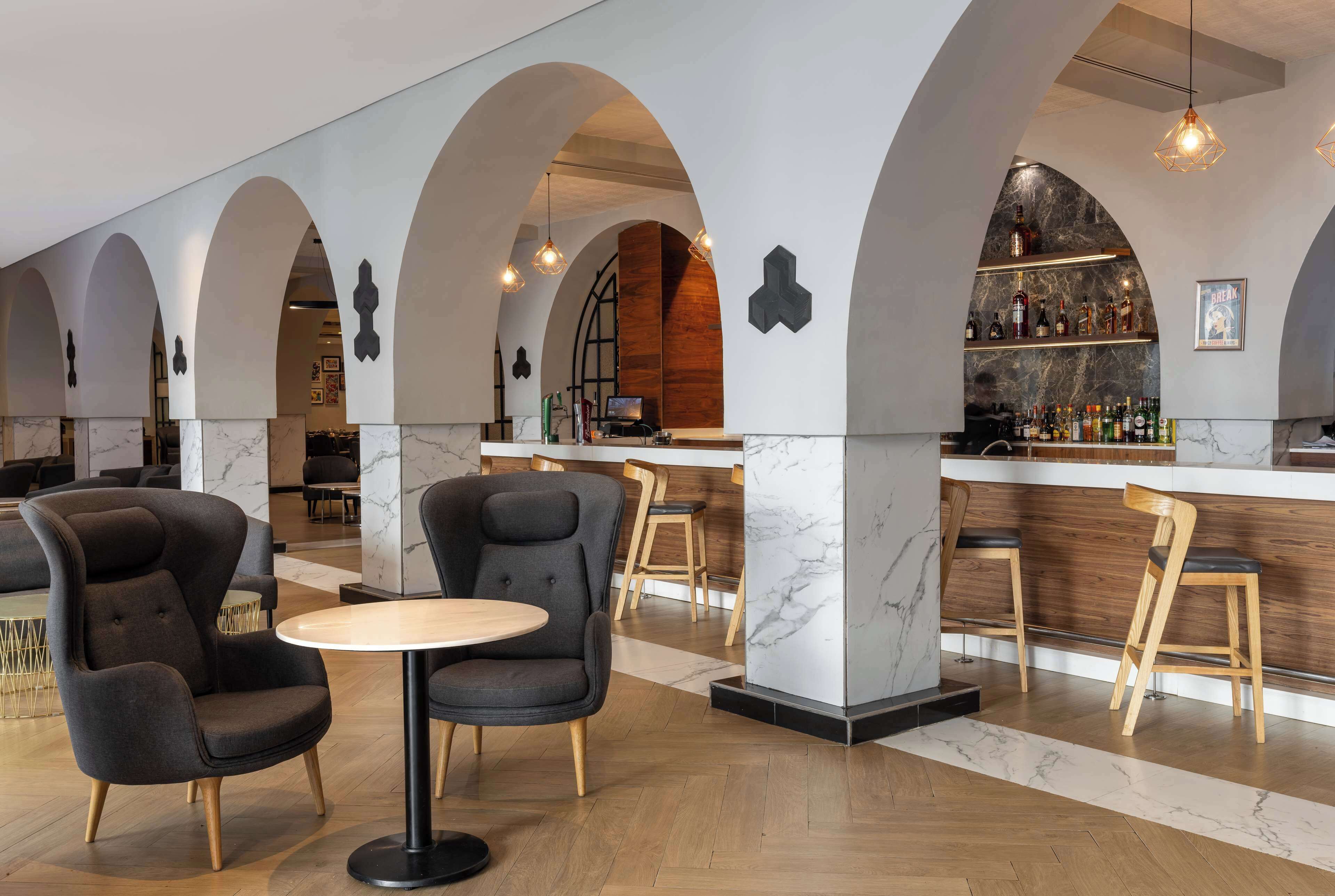 A modern bar area with marble countertops, wooden chairs, and a central round table.