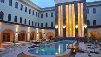A luxurious hotel courtyard with a central swimming pool, multiple arches, and a large building with vertical lighting.