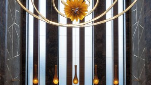 Un vestíbulo con una lámpara moderna, luminarias verticales y suelo de mármol.