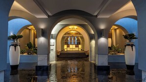 Un hall amplio con suelo de mármol, techos abovedados y una escalera central que lleva a la recepción.