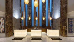 Un área de recepción con suelo de mármol, un mostrador de recepción y una pared azul con líneas verticales.