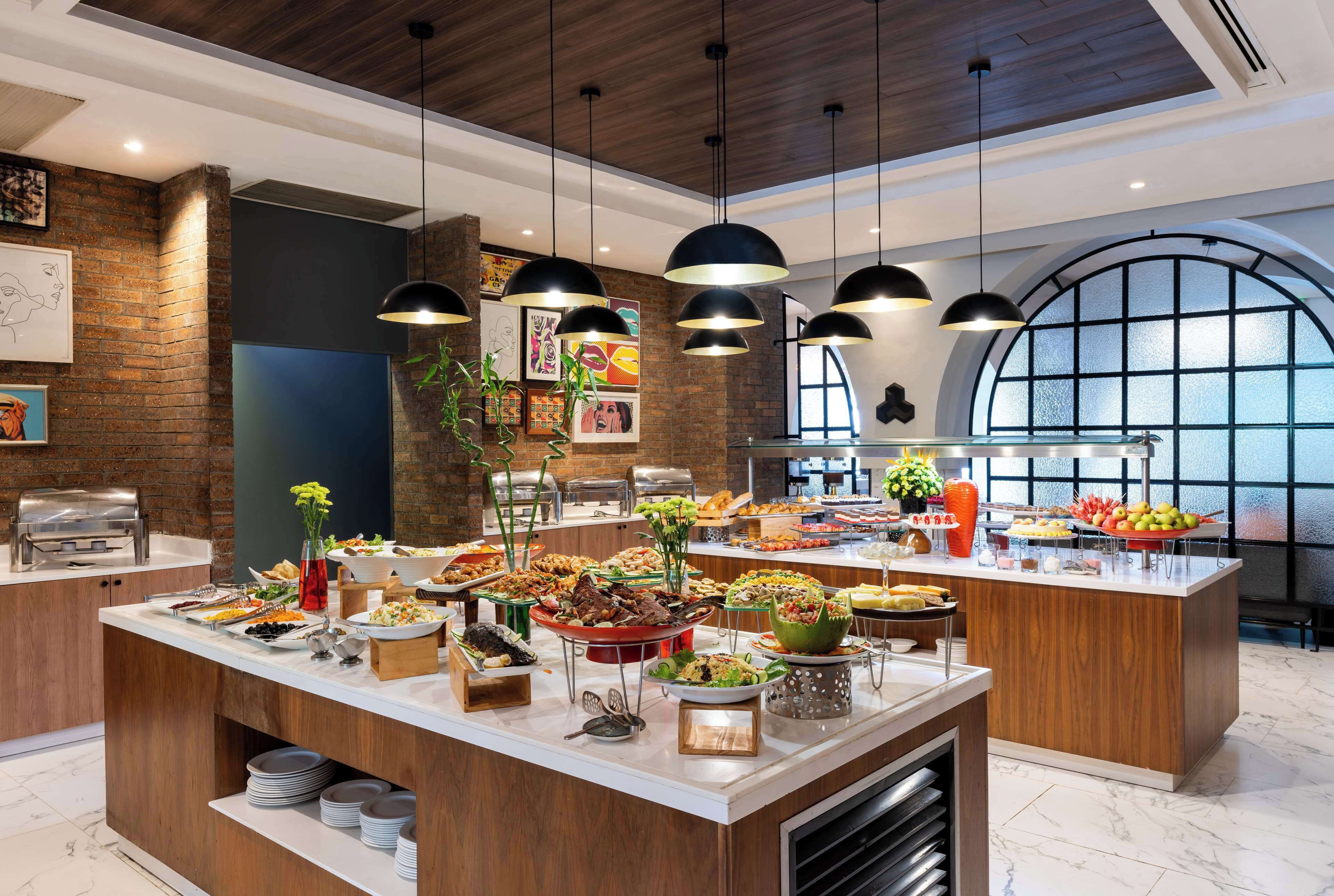 A buffet setup with various food items, a brick wall, and hanging pendant lights.