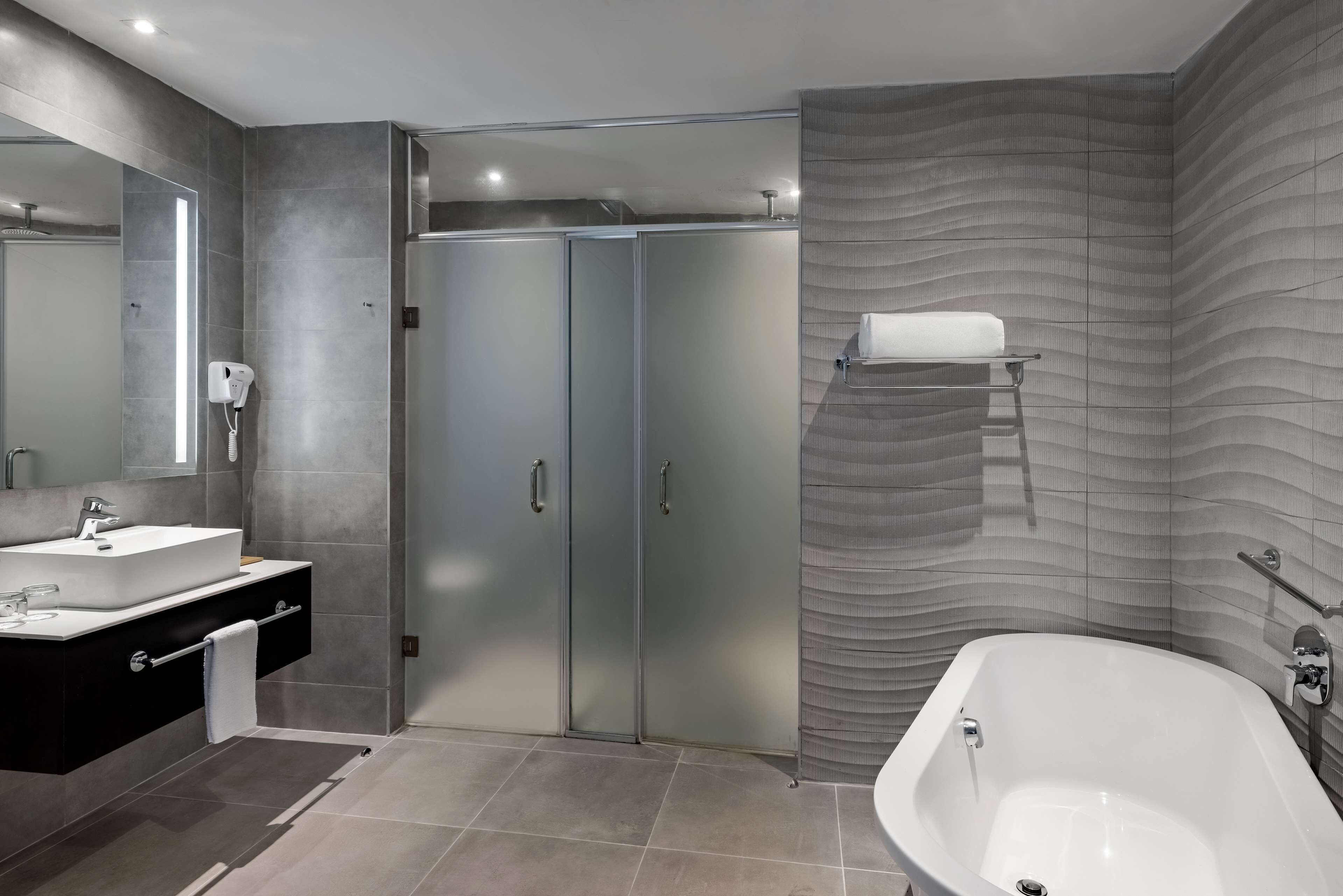A modern bathroom with a large bathtub, a walk-in shower, and a vanity with a mirror.