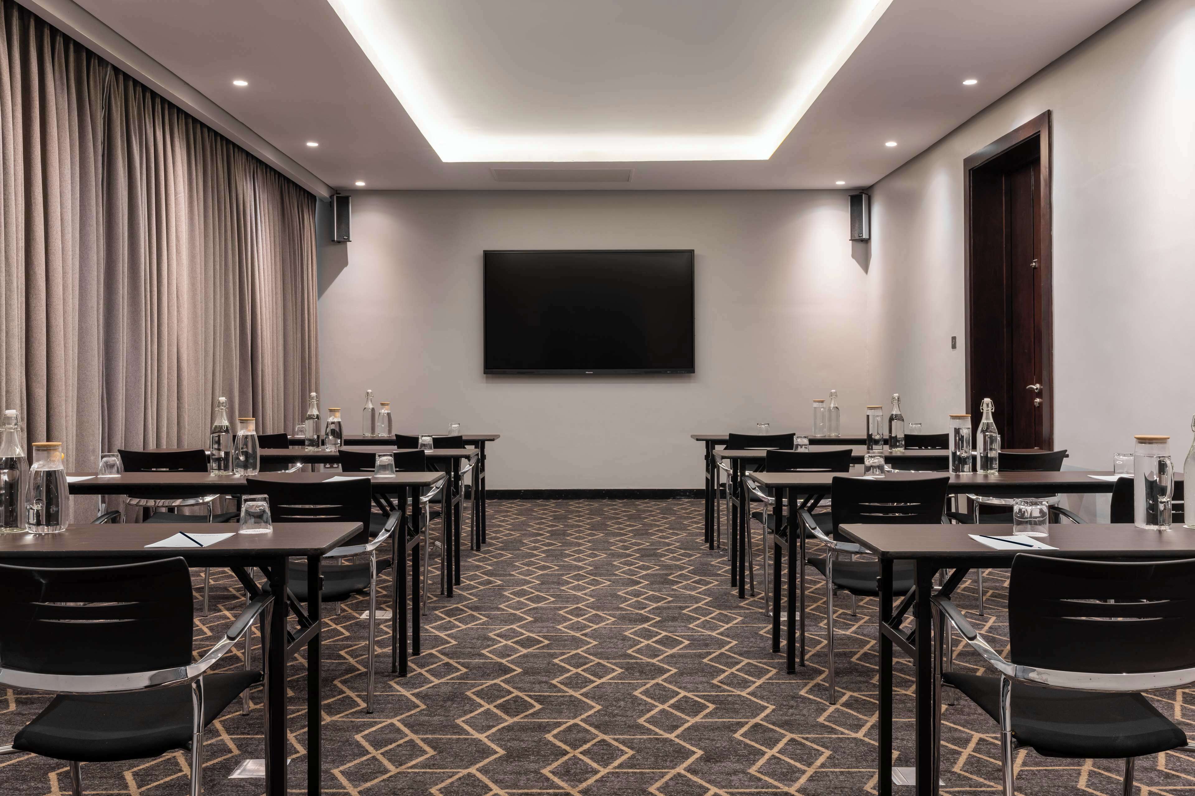 A conference room with a large flat-screen TV, multiple tables with chairs, and a patterned carpet.