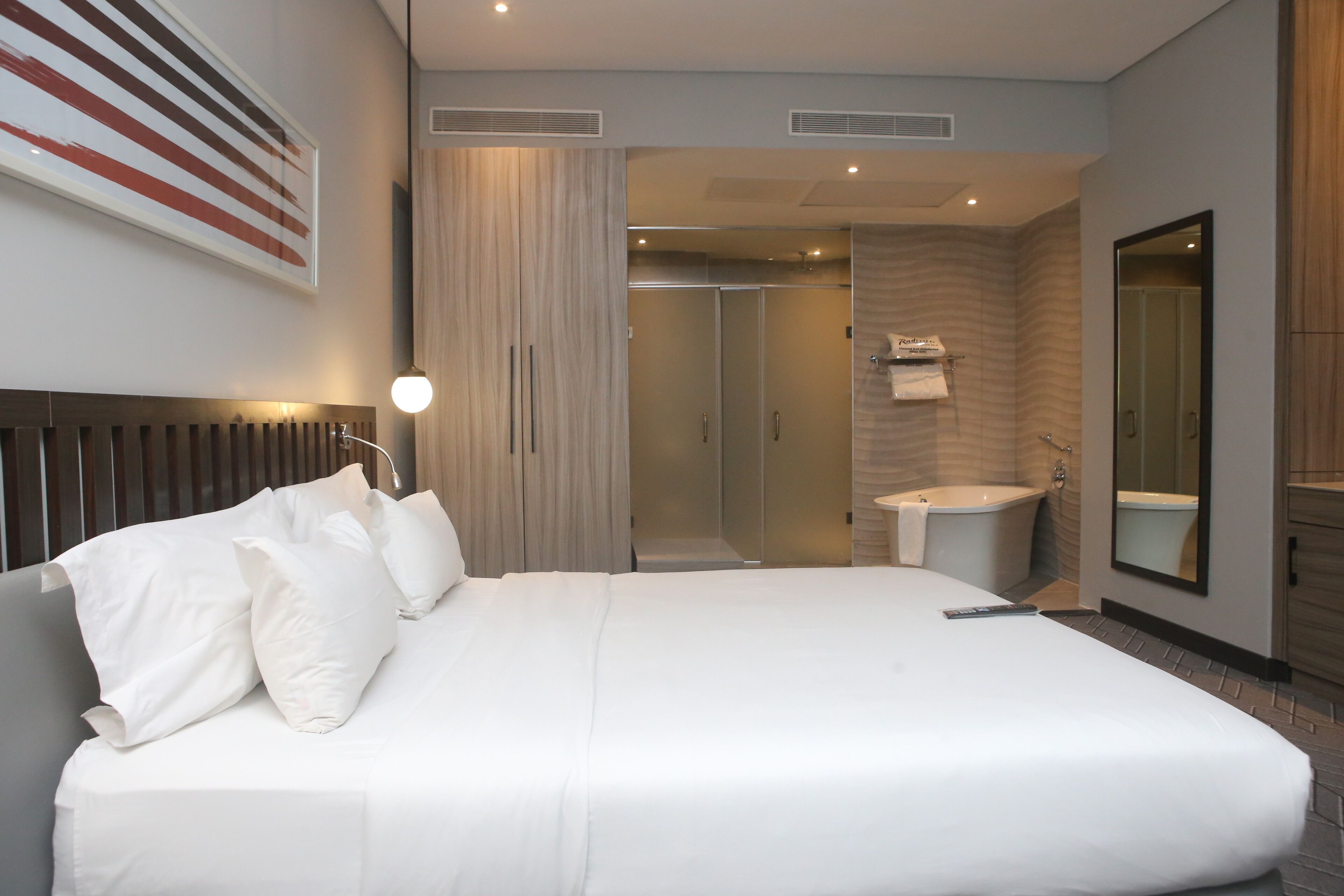 A modern hotel room with a large bed, a bathroom with a bathtub, and a shower.