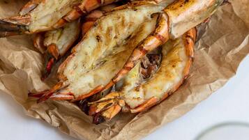 Gambas a la parrilla en una bandeja forrada con papel, junto con recipientes pequeños de pimienta negra y chiles rojos, y una copa de vino blanco.