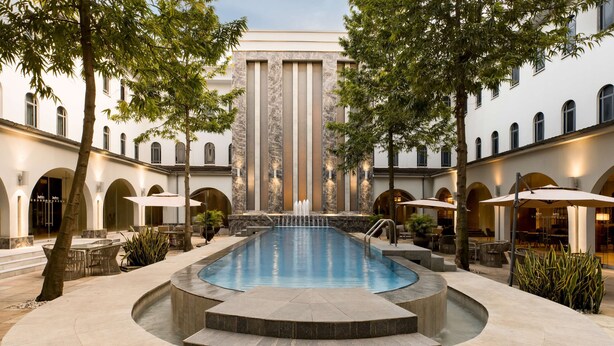 Zona de piscina con escalones que bajan al agua, rodeada de mobiliario exterior y árboles.