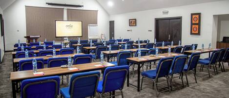 Un salón de conferencias con filas de mesas y sillas, equipado con botellas de agua y tarjetas de identificación.