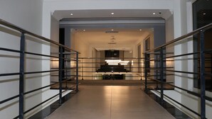 En moderne hotelgang med en central trappe, et godt oplyst reception og udsigt til et rummeligt værelse.