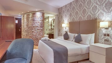 A hotel room with a stone accent wall, a bed with a headboard, bedside tables, a desk, and a chair.