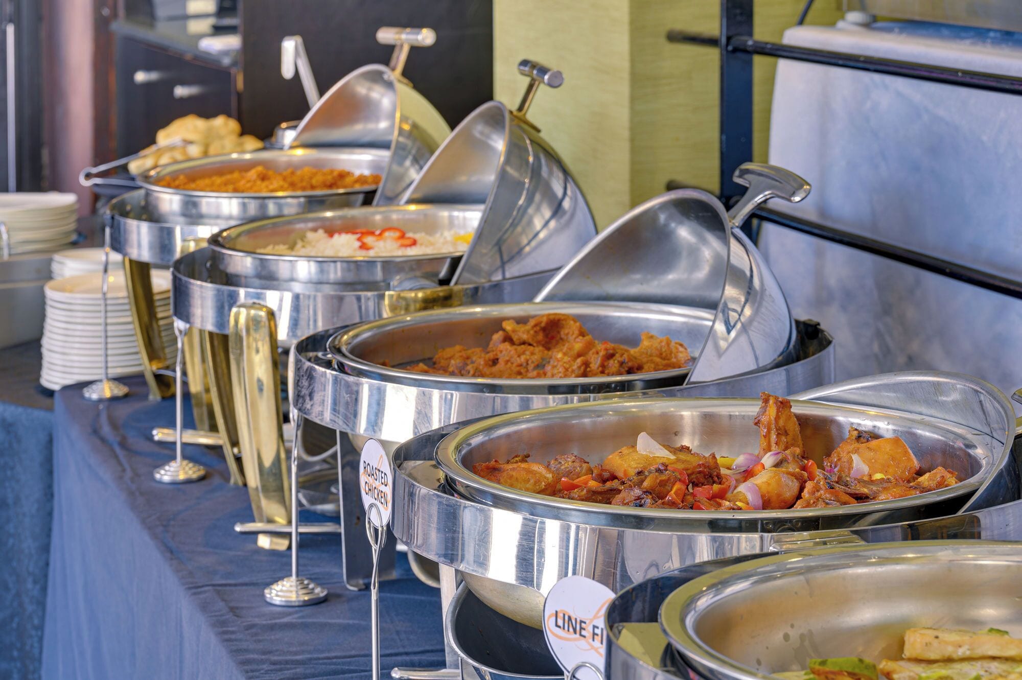 A buffet with various dishes, including roasted chicken and other prepared foods, served in stainless steel containers.