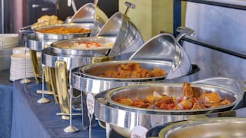 A buffet with various dishes, including roasted chicken and other prepared foods, served in stainless steel containers.