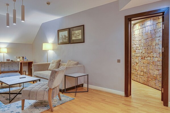 A modern living room with a sofa, coffee table, and lamp. There is a stone wall and a door leading to another room.