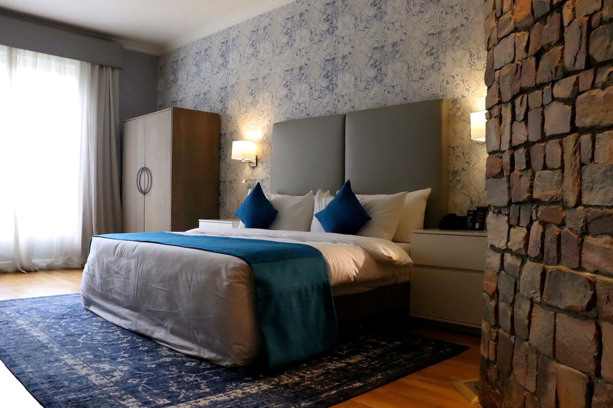 Habitación de hotel con una cama grande, cabecera, mesita de noche, armario y una pared decorativa de ladrillo.