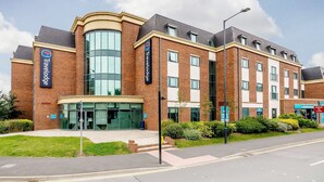 Un hotel Travelodge con fachada de ladrillo moderno, ventanas grandes y una entrada de cristal curva.