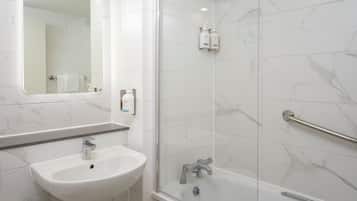 Een moderne badkamer met een witte wastafel, een douche met glazen wand en een betegelde muur van marmer.
