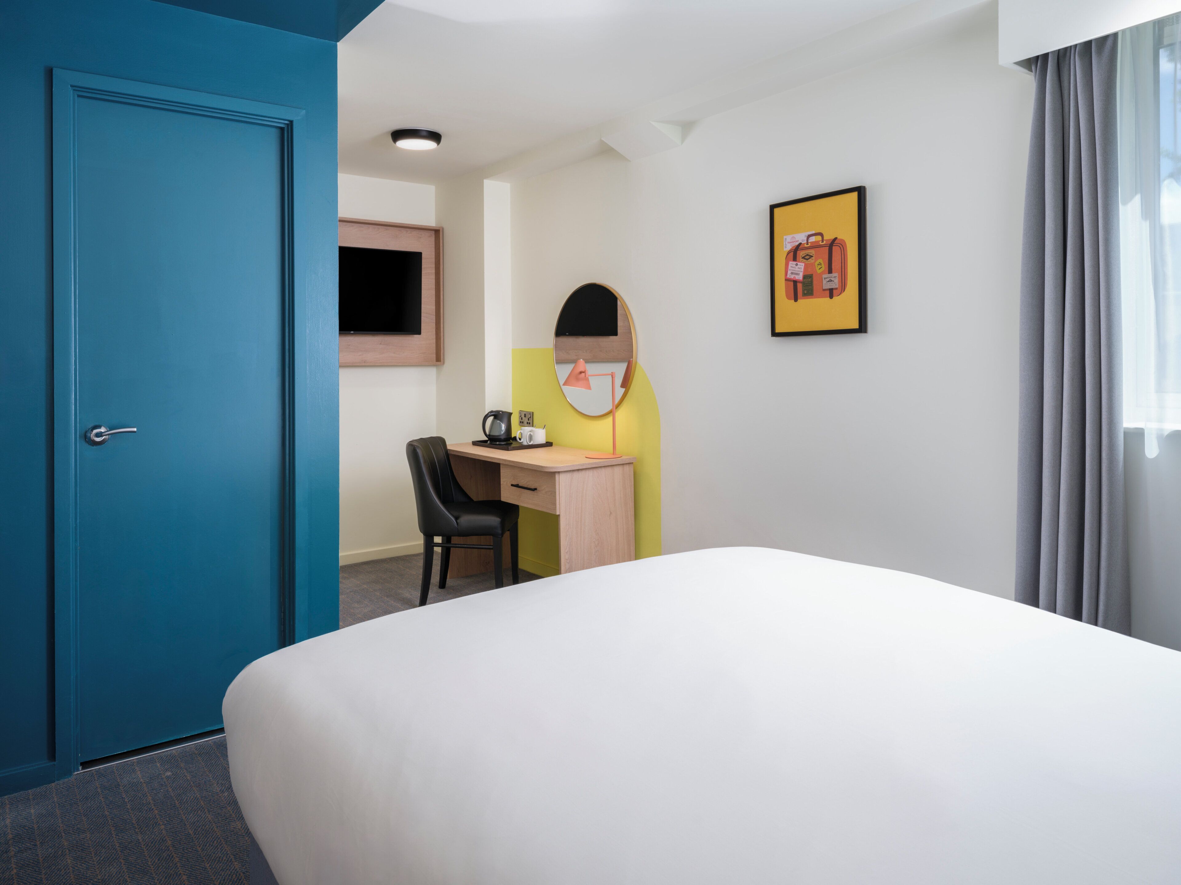 A hotel room with a bed, a desk, a chair, a television, and a framed picture on the wall.
