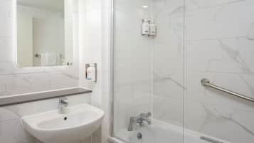 Un baño con lavamanos blanco, espejo, ducha y azulejos de mármol.