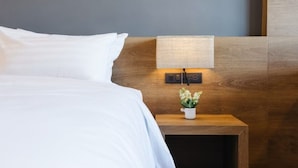 A neatly made bed with white linens, a wooden nightstand with a small potted plant, and a wall-mounted light fixture.