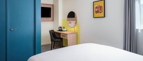A hotel room with a bed, a desk, a chair, a television, and a framed picture on the wall.