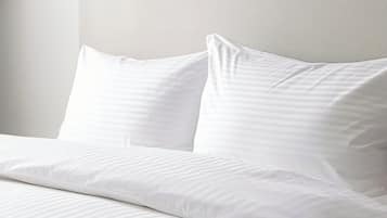 Una cama bien tendida con sábanas y almohadas blancas.