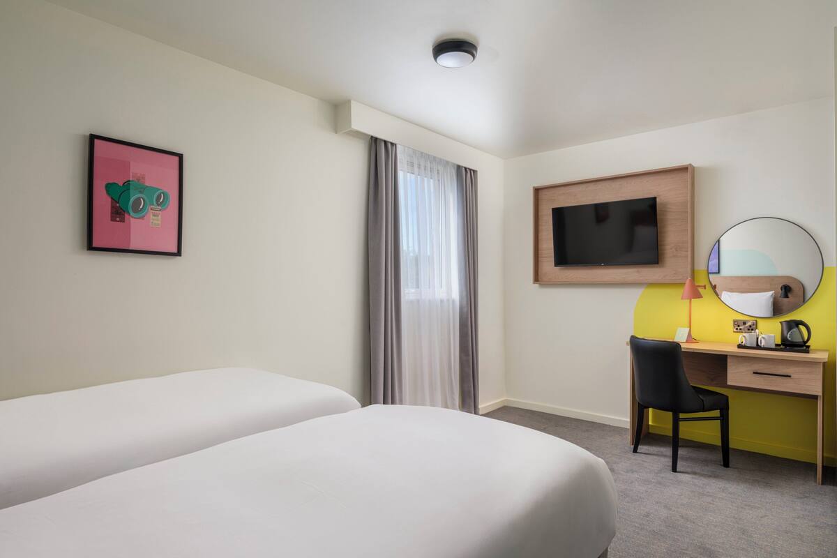 A hotel room with two beds, a desk with a chair, a television, a mirror, and a picture on the wall.